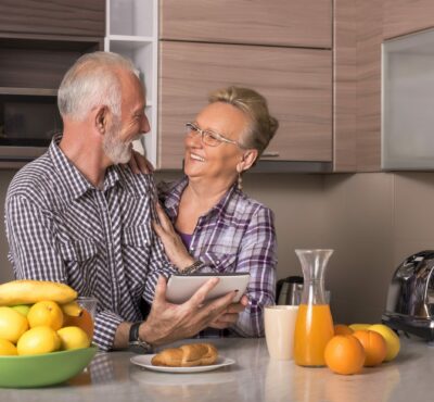 An elderly retired couple watching a video together on a tablet in a kitchen