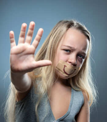 Sad and frightened little girl with bloodshot and bruised eyes, fiction of happiness Sad and frightened little girl with bloodshot, bruised eyes and false smile on her mouth. Concept of child violence, domestic abuse. Depressed being victim of parents. Illusion of happy childhood.