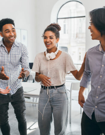 Funny african girl in vintage jeans posing between black and asian friends in international university. Freelance specialists meeting with foreign colleagues.