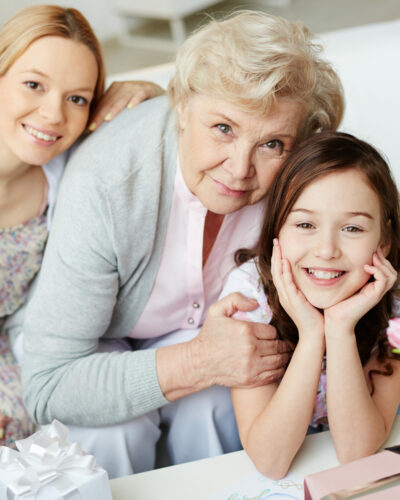 Portrait of happy little girl, her mother and grandmother looking at camera at home